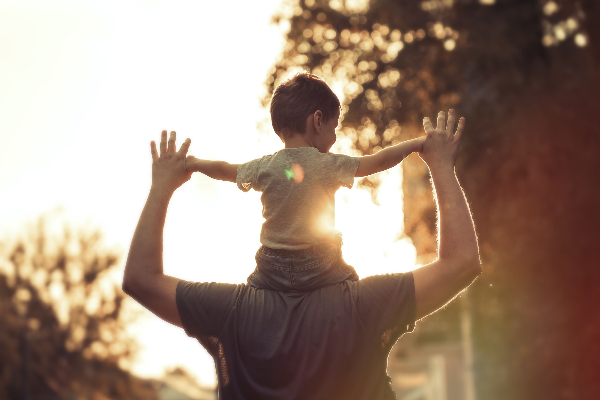 Young father with his little child sitting on father's shoulders in Summer in City